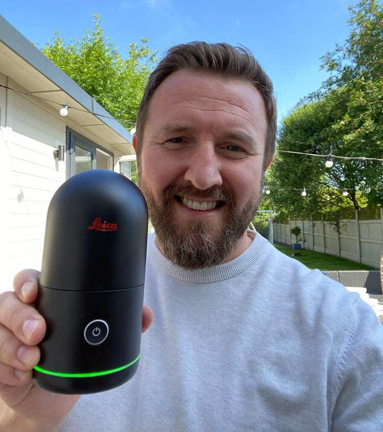 Paul Burrows standing outside holding a BLK360 to the camera