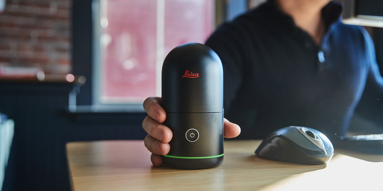 person sitting at a computer desk with a BLK360 in their hand