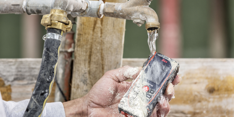 A dirty Leica DISTO X3 is cleaned under a jet of water. 